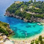A panoramic view of Paleokastritsa bay in Corfu with turquoise water, green cliffs, and small boats floating in clear sea.