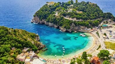 A panoramic view of Paleokastritsa bay in Corfu with turquoise water, green cliffs, and small boats floating in clear sea.