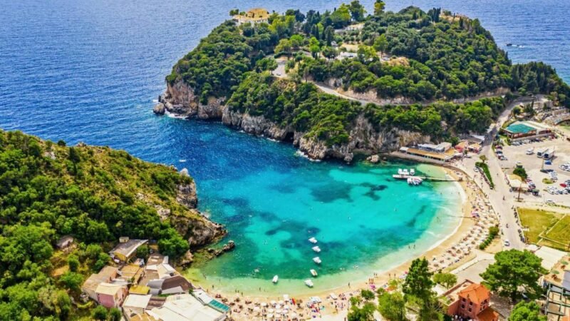 A panoramic view of Paleokastritsa bay in Corfu with turquoise water, green cliffs, and small boats floating in clear sea.