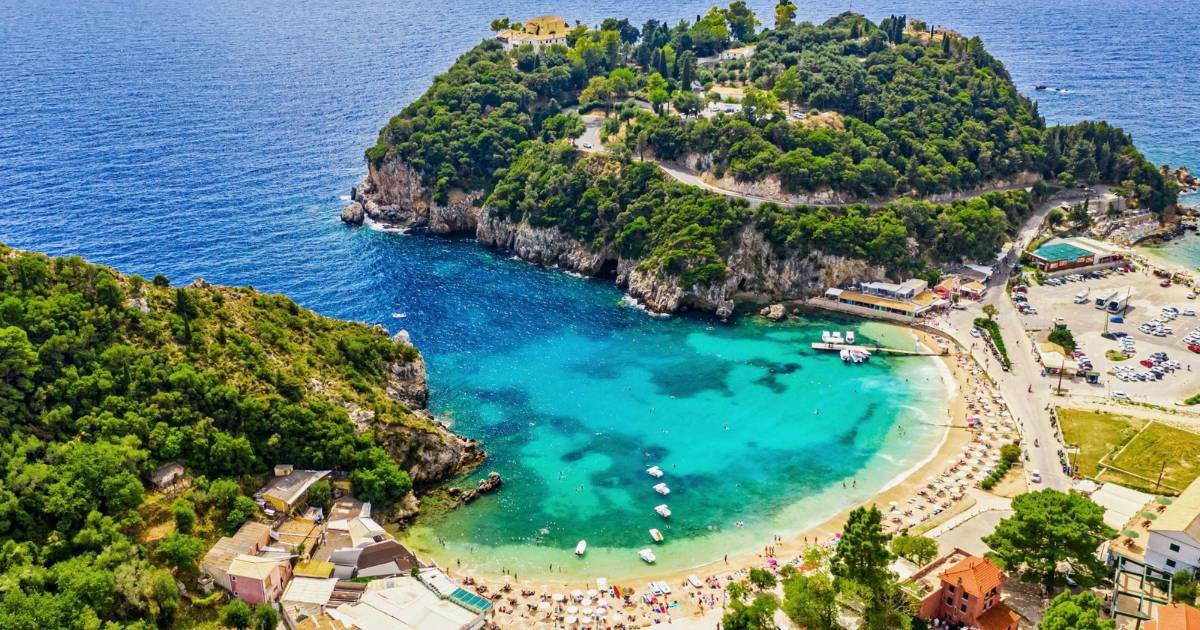 A panoramic view of Paleokastritsa bay in Corfu with turquoise water, green cliffs, and small boats floating in clear sea.