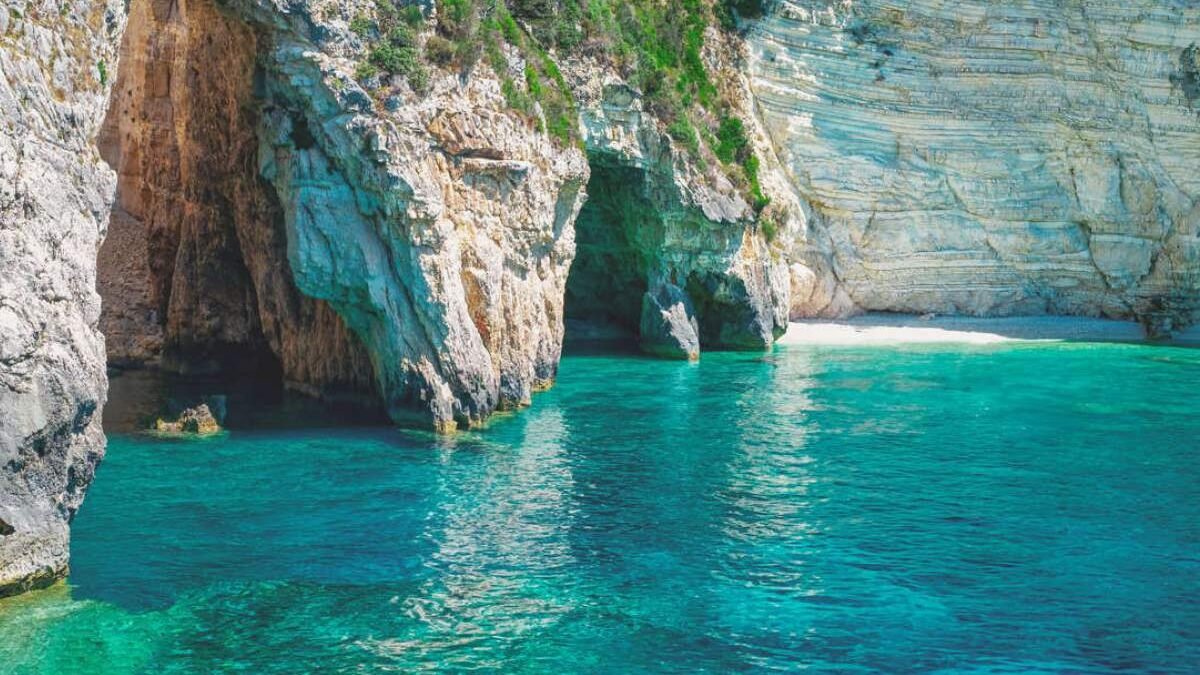 Boat entering sea caves along the cliffs of Paleokastritsa with bright blue water reflecting inside the cave.