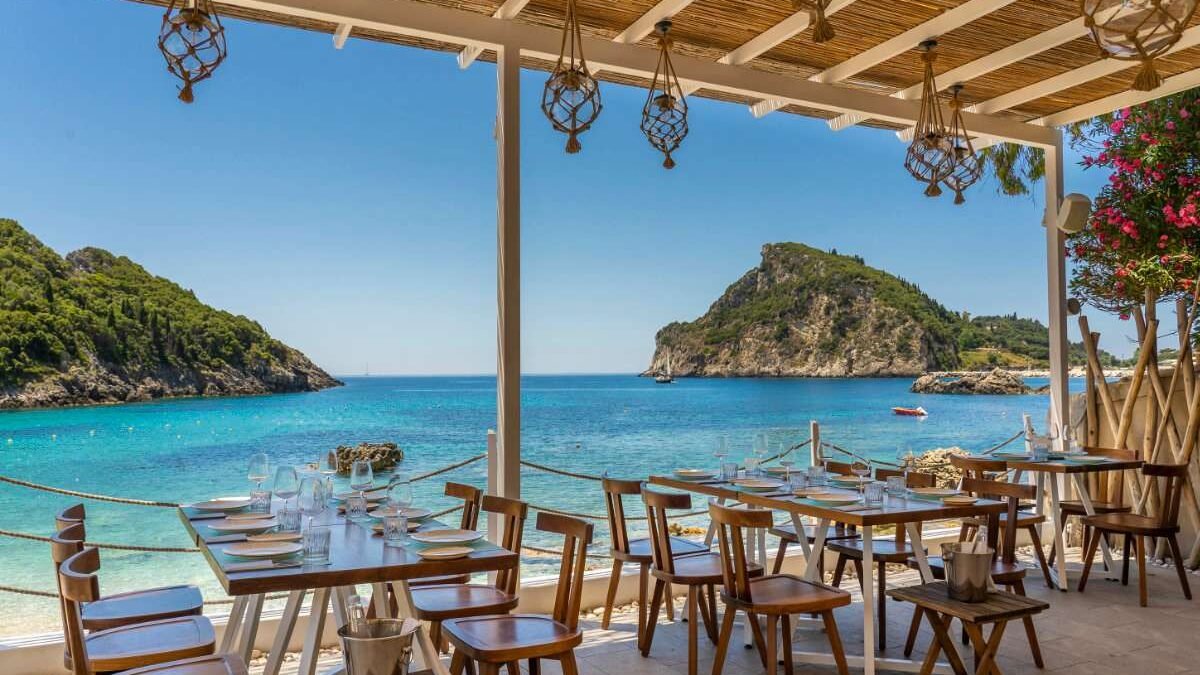Taverna by the sea in Paleokastritsa with tables facing the bay and boats in the background.