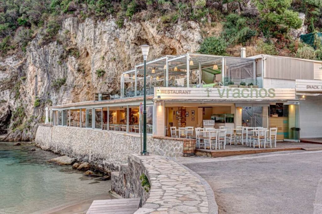 Seaside restaurant Vrachos in Paleokastritsa with panoramic view over turquoise bay and cliffs in Corfu.