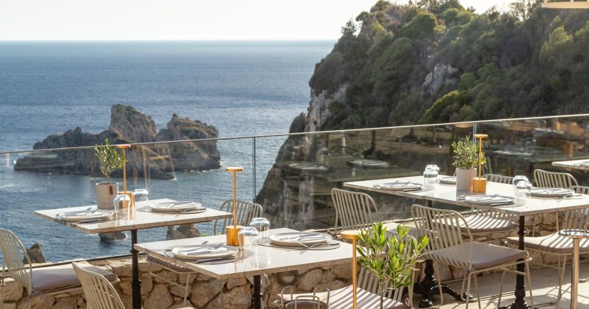 Seaside view of Paleokastritsa bay in Corfu with tavernas overlooking turquoise water and boats in the distance.