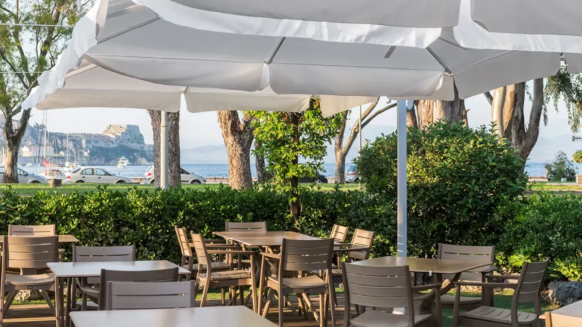 Quiet courtyard restaurant in Corfu Town with greenery, wooden tables, and soft evening lighting.