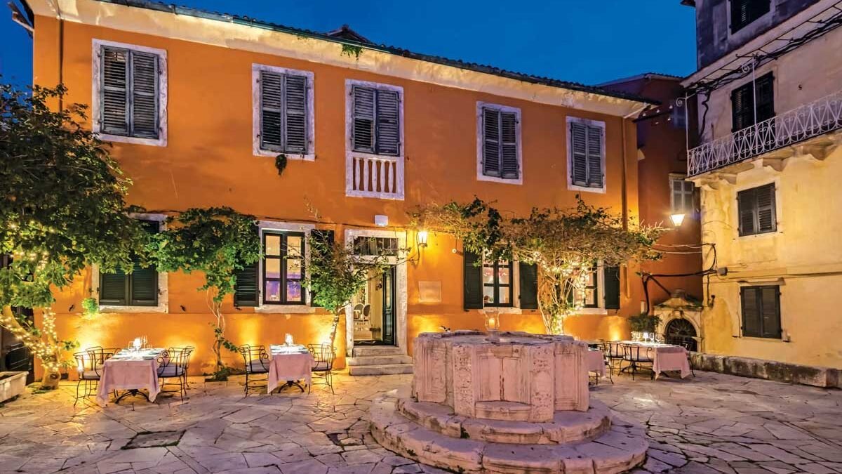 Romantic outdoor restaurant in Corfu Town with warm lights, stone square, and elegant table setup at night.