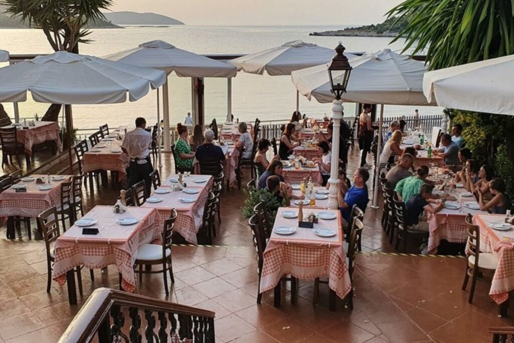 Outdoor terrace at Janis Taverna in Kassiopi, Corfu, overlooking the Ionian Sea and surrounding coastline.