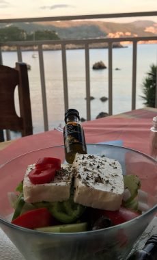 Greek grilled meat platter served at tavern with sea view in background.